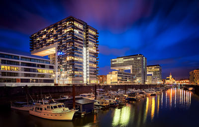 Boats moored in canal by illuminated buildings against sky at night