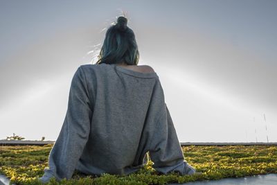 Rear view of woman sitting on field against clear sky