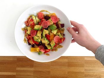 High angle view of hand holding salad bowl on table