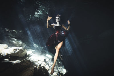 Woman with face paint by rock formation underwater