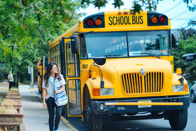 Full length of woman walking by school bus on road