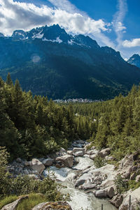 Evergreen forest with snowy mountains, village and blue sky in argentiere, france.