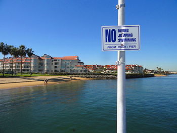 Information sign by sea against clear blue sky