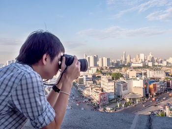 Young woman photographing on city buildings against sky