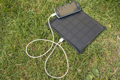 High angle view of smart phone getting charged on field