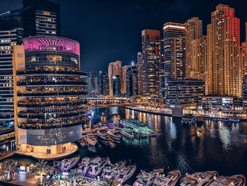 Illuminated buildings by river against sky in city at night