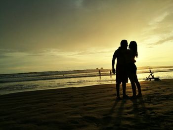 Silhouette friends on beach against sky during sunset