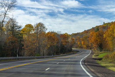 Road amidst trees against sky during autumn