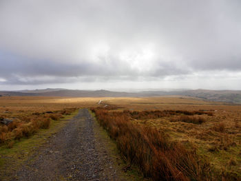 Dirt road amidst field against sky