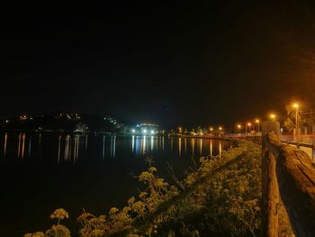 Illuminated city by river against sky at night