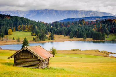 Hut on field by lake against mountains