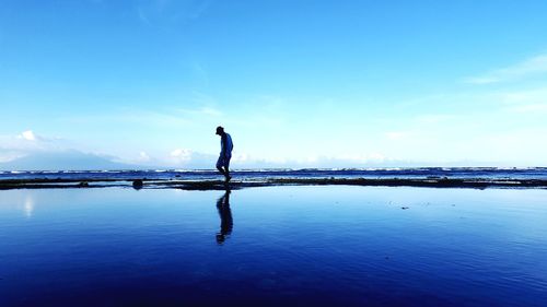 Man standing on beach against blue sky