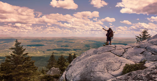 Man with arms outstretched standing on mountain against cloudy sky