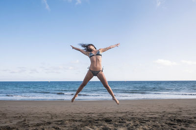 Full length of woman jumping at beach against sky