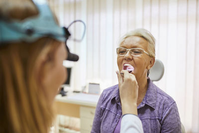 Ent physician examining mouth of a senior woman