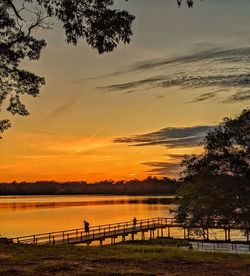 Orange and yellow sunset over a lake with fishing pier and silloettes 