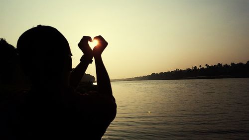 Rear view of silhouette man in lake against sky during sunset