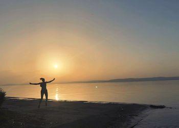 Silhouette man standing at beach against sky during sunset