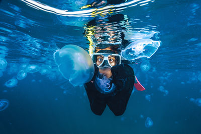 A woman in a black wetsuit is in the water with jellyfish. the jellyfish are floating around her