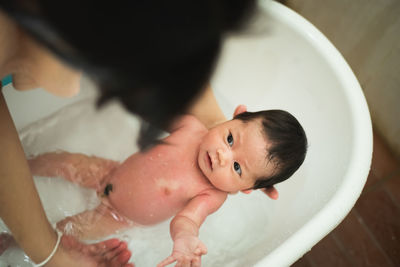 Cropped hands of mother holding naked newborn daughter in bathtub