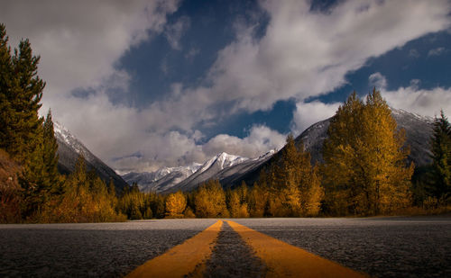 Road by trees on mountain against sky