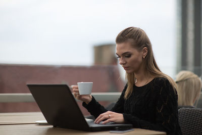 Young woman using laptop while sitting at sidewalk cafe