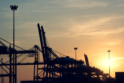 Silhouette cranes at construction site against sky during sunset