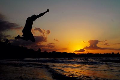 Silhouette man jumping at beach during sunset