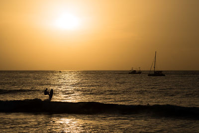 Silhouette people on sea against sky during sunset