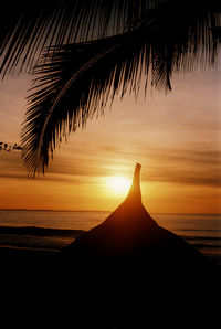 Silhouette palm tree on beach against sky at sunset