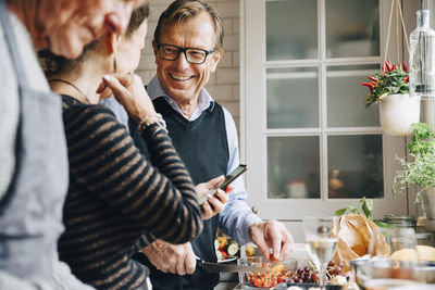 Smiling man looking at woman standing by friend in kitchen