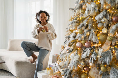 Side view of woman holding christmas tree at home