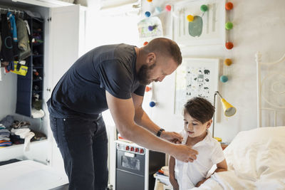 Man dressing son in bedroom