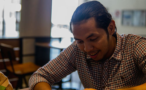 A portrait of young asian malay businessman sitting inside of cafe and looking at phone.