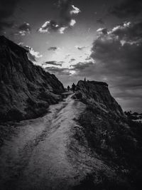 Road passing through mountain against cloudy sky