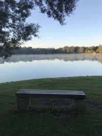 Bench on field by lake against sky