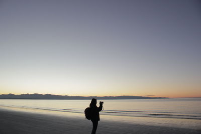 Silhouette man standing on beach against clear sky during sunset