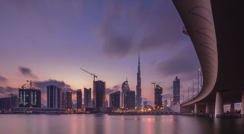 Modern buildings by river in city at dusk