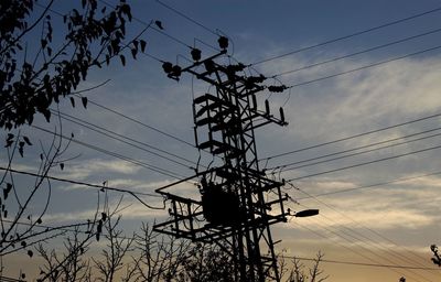 Low angle view of silhouette electricity pylon against sky at sunset