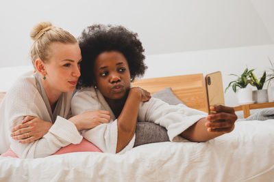 Portrait of smiling friends sitting on bed at home