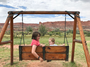 Full length of girl sitting on wood against sky
