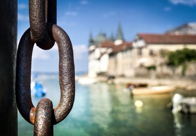 Close-up of rusty chain by river against sky