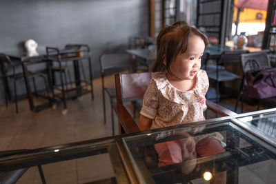 Thoughtful baby girl sitting on chair in restaurant