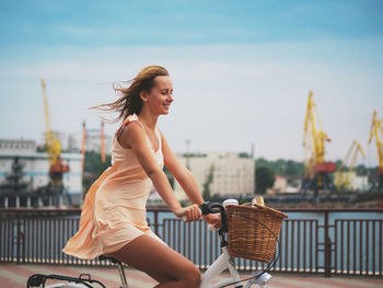 Portrait of smiling young woman in city against sky