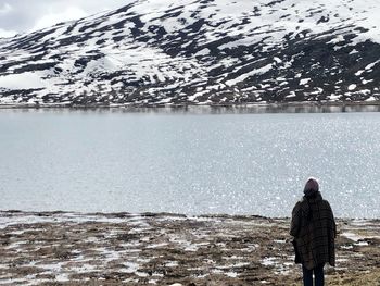 Rear view of person standing by lake during winter