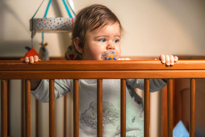 Cute boy with pacifier by railing at home