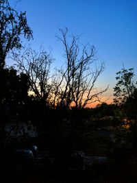 Silhouette trees on field against clear sky at sunset