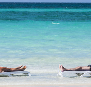 Low section of friends relaxing on lounge chairs at beach