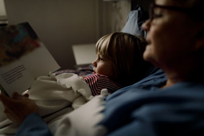 Grandmother reading story book for grandson on bed at home