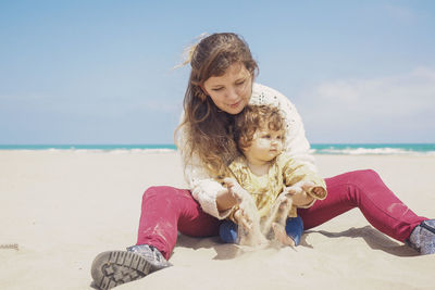 Happy woman sitting on shore at beach against sky